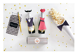 Champagne fiasco party favors with tuxedo and dress and mustache and lipstick and popcorn and a voting ballot with pencil on a white itemization with confetti and cake truffles in a box